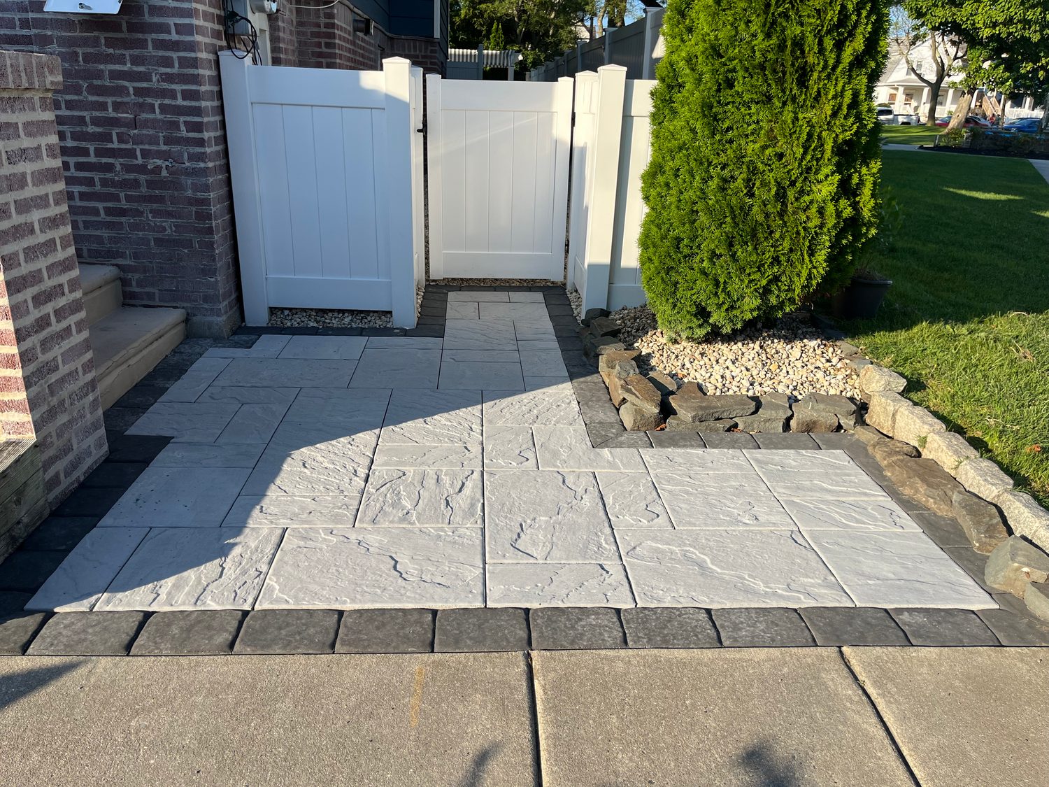Stamped concrete patio with a decorative center medallion beside a brick home and white fence