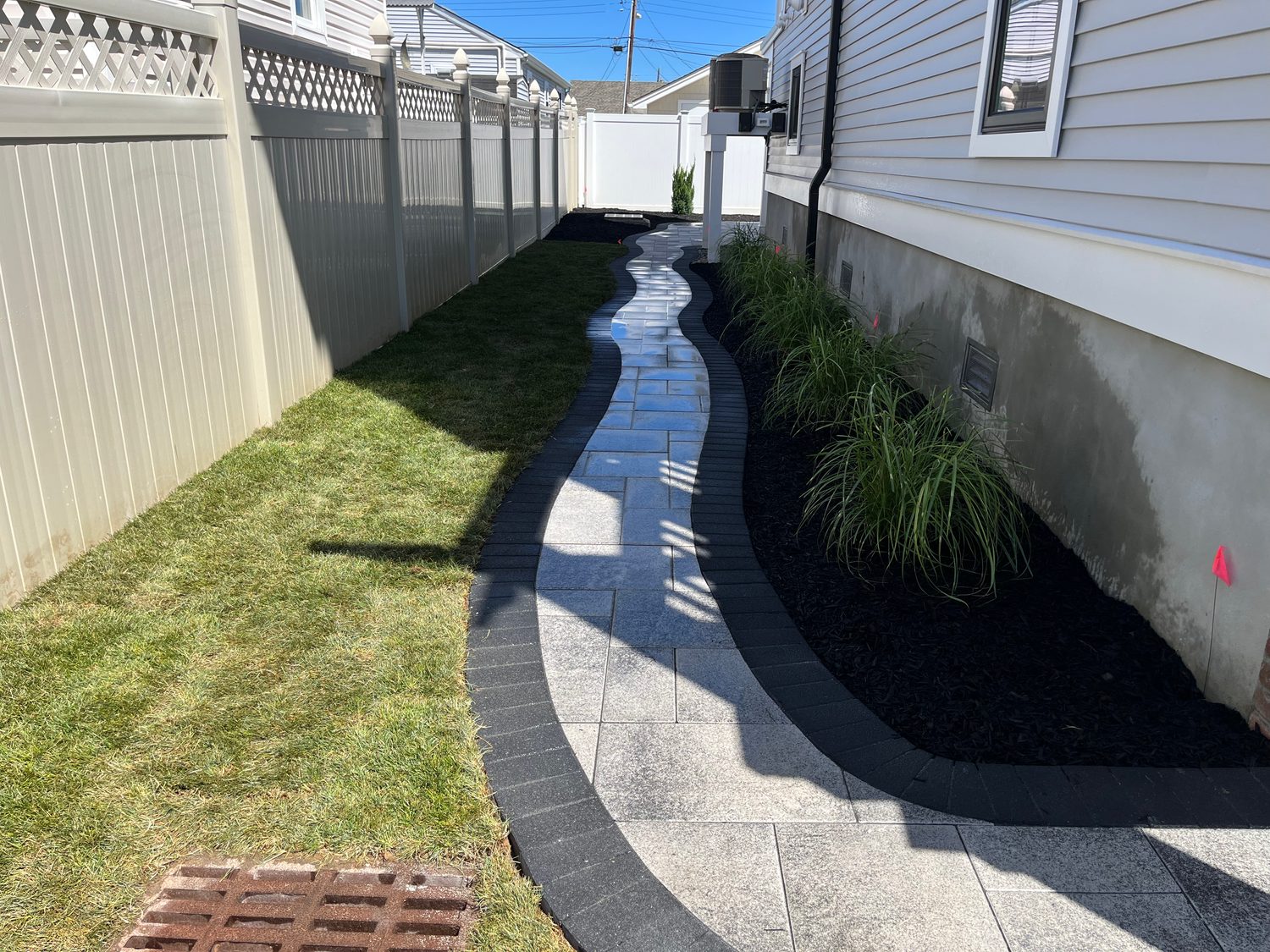 Curved paver walkway running down a side yard beside a planted mulch bed and green lawn